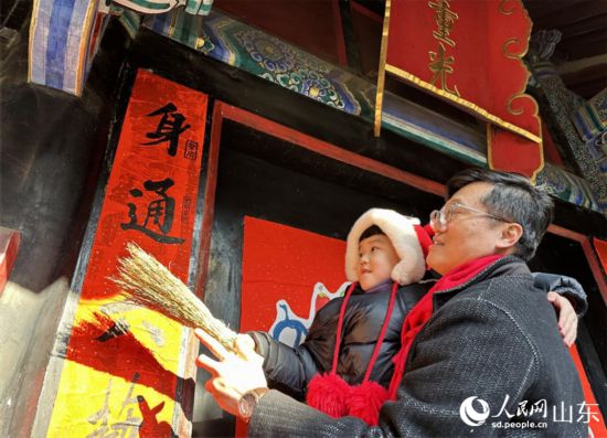 春節(jié)前，孔子后裔在孔府重光門前貼春聯(lián)。 人民網(wǎng) 喬姝攝